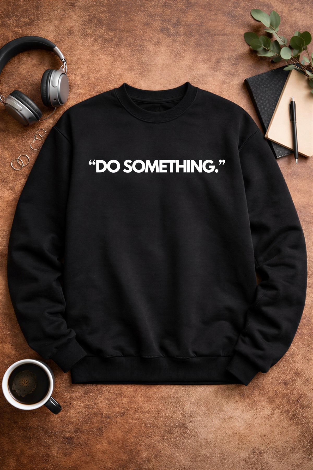 a black sweatshirt with the phrase "Do something" printed on it, along with a pair of headphones, a notebook, a pen, and a plant.